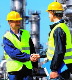 Two petrochemical contractors closing a deal in front of an oil refinary